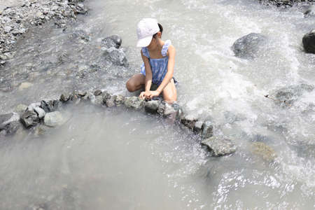 Japanese student girl damming river by stone (7 years old)の写真素材