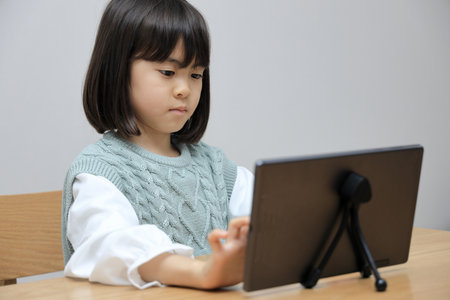 Japanese student girl using a tablet PC in dining room (8 years old)の写真素材
