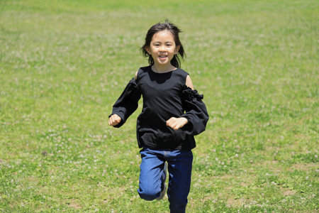 Japanese student girl running on the grass (8 years old)の写真素材