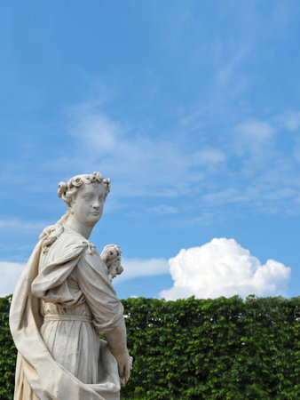 Classic marble statue of Flora isolated on background of blue sky with clouds and green plantsの写真素材