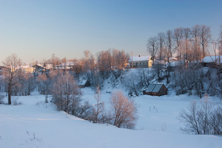 Winter village landscape with snow-covered houses and trees under blue skyの写真素材