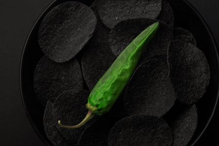 Black chips and green hot peppers on black background