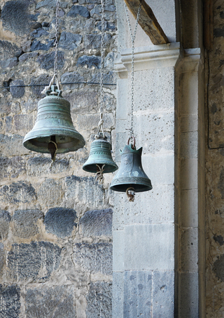 three church bells of small, medium and large size hanging in chainsの写真素材