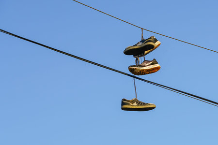 Several tennis shoes on power lines in front of a clear blue sky.