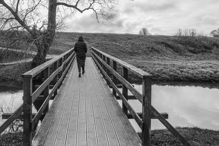 woman in black coat crosses wooden bridge, depressed view