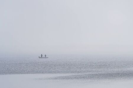 view of the lake and a boat with anglers in the fogの写真素材