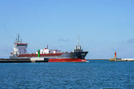 a cement transport vessel enters the port through breakwater gates equipped with navigation signal towersの写真素材