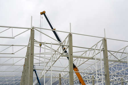 a crane with a telescopic boom in the assembly of metal structures in a new modern industrial buildingの写真素材