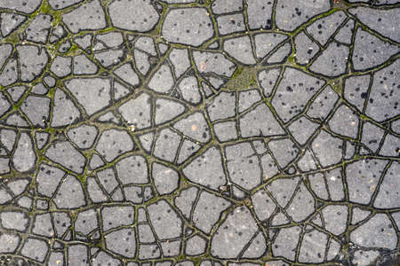 worn and cracked in many small fragments old grey asphalt surface backgroundの写真素材