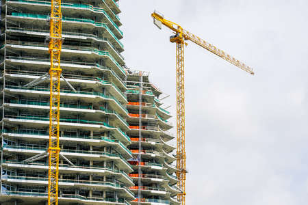 a yellow tower crane and a fragment of the facade of an unfinished high cement building or skyscraperの写真素材