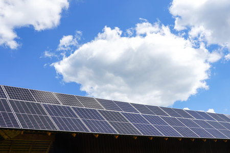 Many photovoltaic solar panels mounted on wooden house roof, background of blue sky with white clouds, roof of solar cellsの写真素材