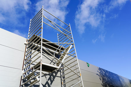 Modern metal scaffolding next to a new building gray sandwich panel facade, blue sky backgroundの写真素材