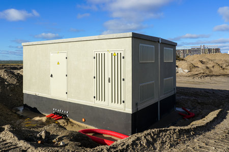 New modern electric transformer room building with grey doors and yellow hazard signs on blue sky background in a new unfinished industrial facilityの写真素材