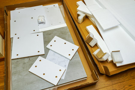 Opened cardboard box with new white and gray laminated chipboard set, fitting kit , fastenings and...