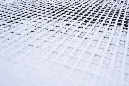 A checkered outline pattern of white snow on dark cobblestones, abstract perspective view on checkered snow textureの写真素材