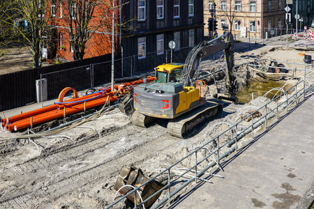 Underground pipeline replacement site with dewatering system on city street, excavator digs deep...