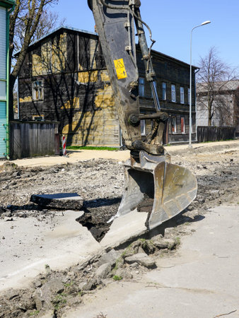 Crawler excavator bucket dismantle the old asphalt layer before the reconstruction of the city...