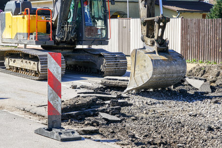 A large crawler excavator with a bucket dismantle the old layer of asphalt before the reconstruction...