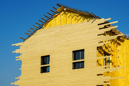 Residential house facade siding works with wooden planks after facade spraying with thermal insulation foam, blue sky backgroundの写真素材