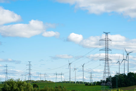 An industrial nature landscape with several high voltage power lines transmission pylons and wind...