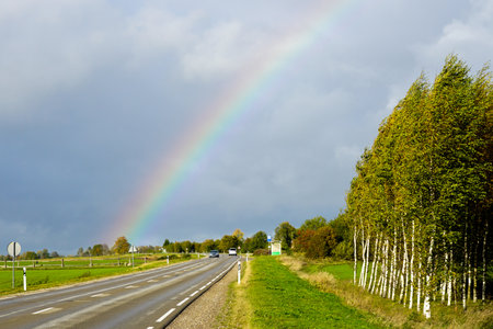 A rainbow of natural colors over a road and a birch grove in a rural area, landscape with colorful rainbowの写真素材