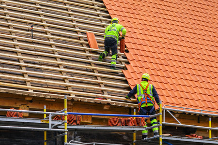 Two roofers in protective workwear installing new clay tiles, new clay tiles layer covering, new clay tile roofingの写真素材