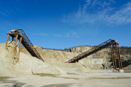 Huge rusty metal structures for transporting rocks in a dolomite mining quarry, gravel crushing, sorting, conveying, blue sky backgroundの写真素材