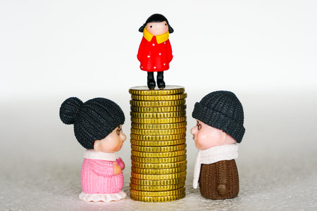 Between elderly grandfather and grandmother toy figures a pile of coins with a child on it, concept and symbol of inheritanceの写真素材