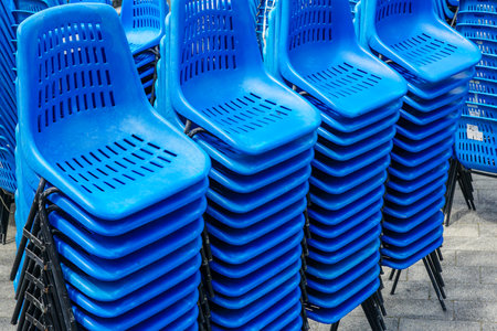 Stacked rows of blue plastic chairs with metal frames for outdoor events on town square, stackable metal framed plastic chairsの写真素材