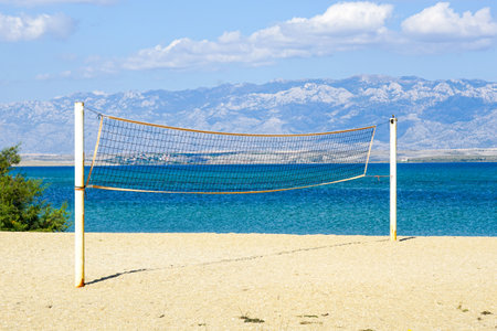 A empty public beach volleyball court with a stretched net against the backdrop of sea, mountains and blue sky, summer sport concept, Croatia, Europeの写真素材
