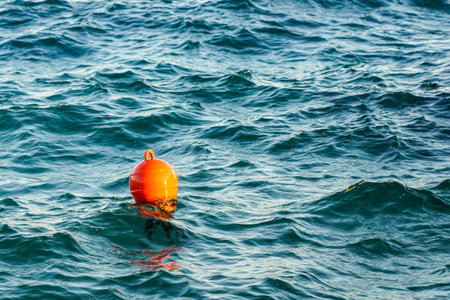 Orange plastic water buoy floating in turquoise sea water, wavy water background