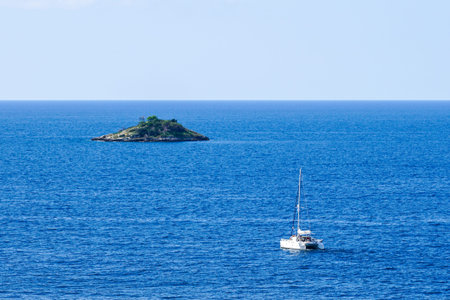 yacht catamaran sailing to a small lonely uninhabited island in the sea, concept of a boat, an uninhabited island and a blue sea to the horizonの写真素材