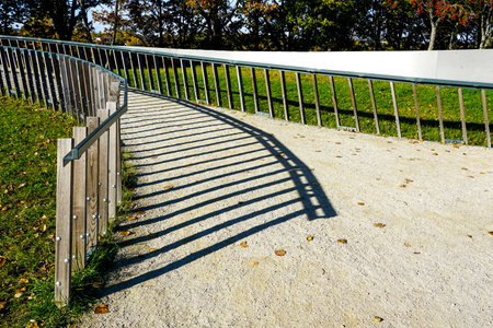 Metal railing casting long shadow lines on the surface of a gravel path in sunny weather, geometric lines pattern of shadows in bright sunlightの写真素材