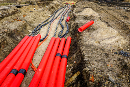 Laying a new underground high-voltage power cable in red corrugated protective tube for the power supply of an industrial facility, cable installationの写真素材