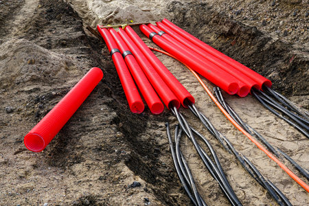 Laying a new underground high-voltage power cable in red corrugated protective tube for the power...