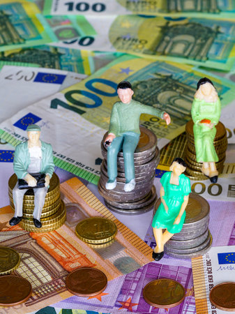 Puppet figures sitting on stacks of coins of different heights, background of money banknotes, concept of relationship between people and moneyの写真素材