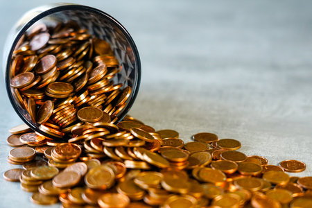 Many coins spilled from an overturned cup, concept of hoarding, savings, success and wealth, cash savings, selected focusの写真素材