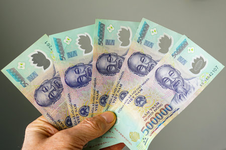 Hand holding five 500,000 dong denominations Vietnamese banknotes with a portrait of Ho Chi Minh on...