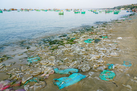Polluted shoreline littered with discarded plastic sacks near fishing boats anchored off a busy Vietnamese coast, Mui Neの写真素材