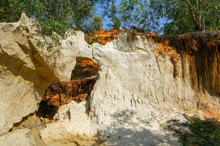 Natural white sandstone arch formation with visible erosion, contrasting red earth, and green trees...