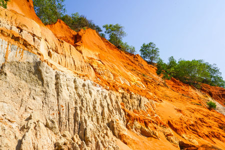 Contrasting red and white sandstone cliffs of Ham Tien Canyon in Vietnam, framed by green trees and...