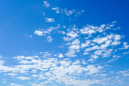 A serene view of the sky shows scattered, fluffy white clouds against a deep blue background on a...