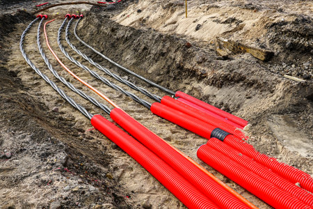 A close-up view of red protective conduits housing underground electrical cables, neatly arranged in a trench during utility installationの写真素材