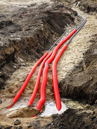 Laying a new underground high-voltage power cable in red corrugated protective tube for the power supply of an industrial facility, cable installationの写真素材