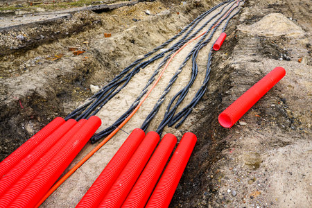 A trench shows underground cable installation in progress with bright red corrugated conduit pipes laid out for protectionの写真素材
