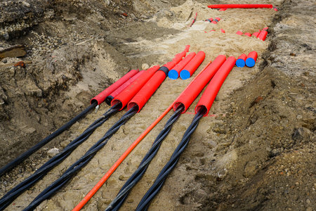 A close-up of electrical power cables laid in a trench with red protective conduits and blue-capped pipes during urban infrastructure workの写真素材