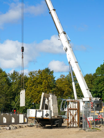 Crane lifts precast concrete wall panel at multi-story residential construction site. Workers and equipment prepare materials for structural assemblyの写真素材