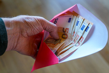 Close-up of a hand holding an envelope filled with 50 euro banknotes, symbolizing savings, salary, pension, financial aid, cash payment, or giftの写真素材