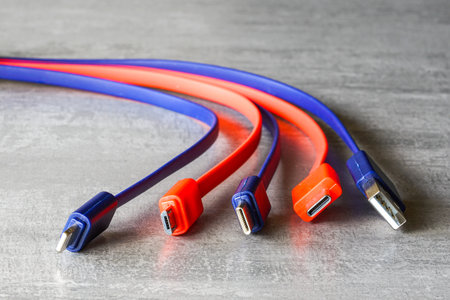 Close-up of red and blue USB and Type-C charging cables on a gray background, symbolizing data transfer, technology, connectivity, and electronicsの写真素材