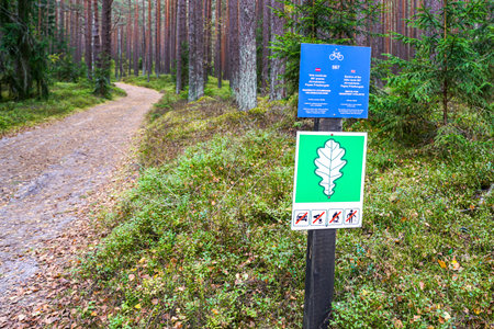 Signpost on a forest trail displays bicycle route info and oak leaf protected area sign with rules against driving, fires, and littering in nature reserveの写真素材